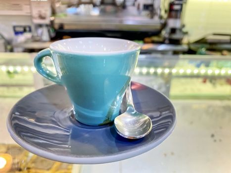 close up of a cup of turquoise coffee on a saucer and with the steel spoon served on the glass counter of an Italian bar. Take a break with a coffee at the bar