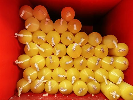 Group of yellow candles with white wicks placed in a red square box. Close-up shooting with low natural light.