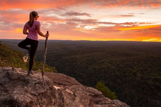 A woman practicing yoga and meditating with positive affirmations while watching beautiful sunset in nature location