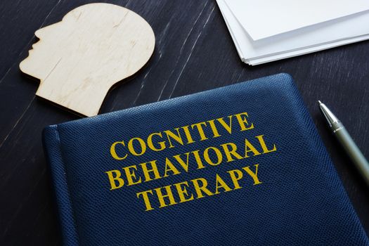 Cognitive behavioral therapy CBT book and wooden head shape.