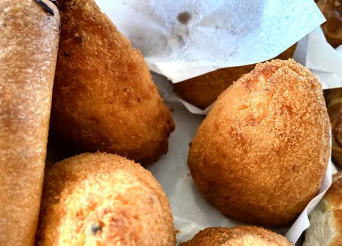 close-up view of a group of arancini, a typical Sicilian dish consisting of a ball of breaded and fried rice and generally stuffed with ragù, peas and caciocavallo cheese, or diced ham and mozzarella