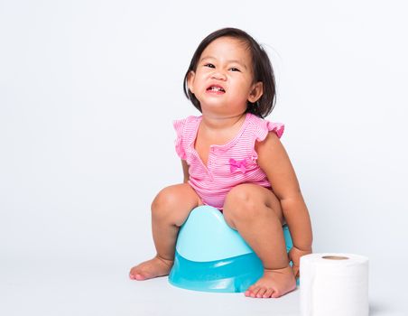 Asian little cute baby child girl education training to sitting on blue chamber pot or potty with toilet paper rolls, studio shot isolated on white background, wc toilet concept