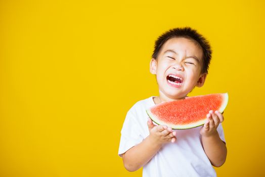 Happy portrait Asian child or kid cute little boy attractive laugh smile playing holds cut watermelon fresh for eating, studio shot isolated on yellow background, healthy food and summer concept