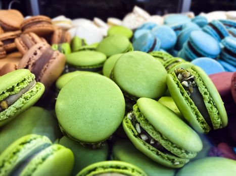 many colorful macarons biscuits arranged disorderly. In the foreground, the green ones with pistachio flavor. Baked cake with various colors