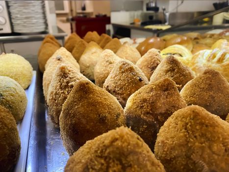 Sicilian arancini arranged on a metal tray and displayed for sale. Typical Sicilian recipe. Famous Italian food. Italian street food