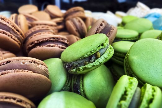 many colorful macaroons biscuits arranged disorderly. In the foreground, the green ones with pistachio flavor. Baked cake with various colors