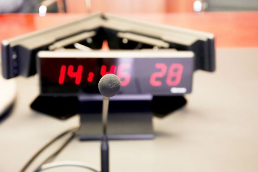 a table microphone on the wooden table of a board in front of a digital clock with red digits. Business and finance.