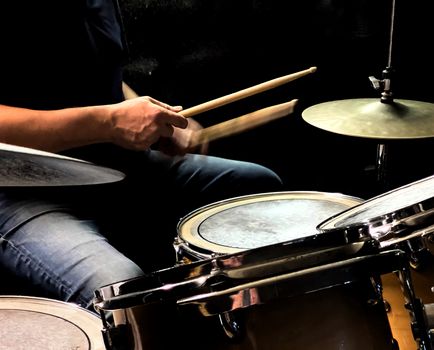 a drummer while playing the drums with wooden sticks in a dark room