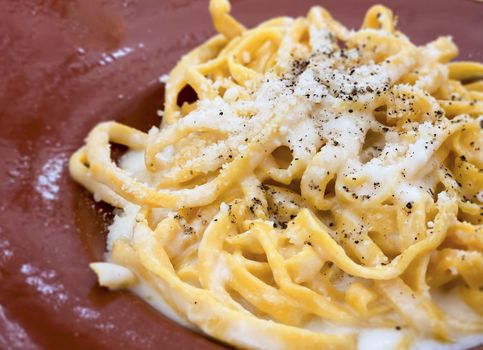 A portion of Italian traditional pasta with cacio e pepe - cheese and pepper- sauce served with grated Parmesan on top