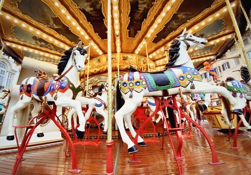 white painted horses in a carousel decorated with lights and gold. Street party and fun