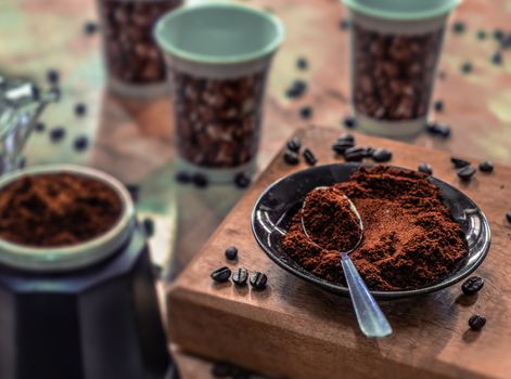 A plate with ground coffee and a spoon on a table, surrounded by coffee stuff