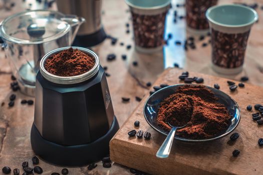 Disassembled coffee maker and a plate with ground coffee on a table, surrounded by coffee stuff