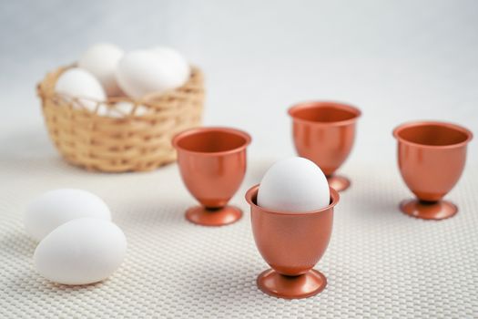 An eggs into a cooper eggs cup and three more empty cooper eggs cup behind it, two eggs beside it.,a basket with eggs at bottom