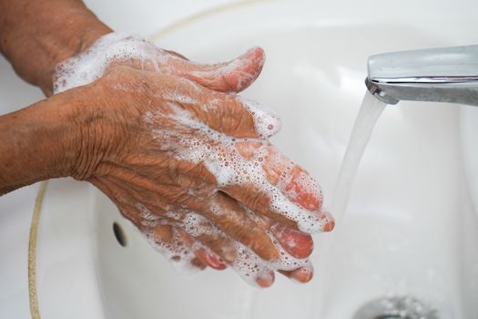 Pair of wrinkled hands washing in a sink