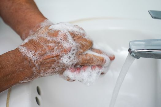 Pair of wrinkled hands washing in a sink