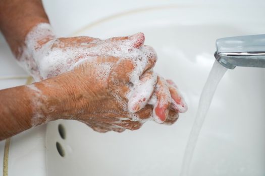 Pair of wrinkled hands washing in a sink