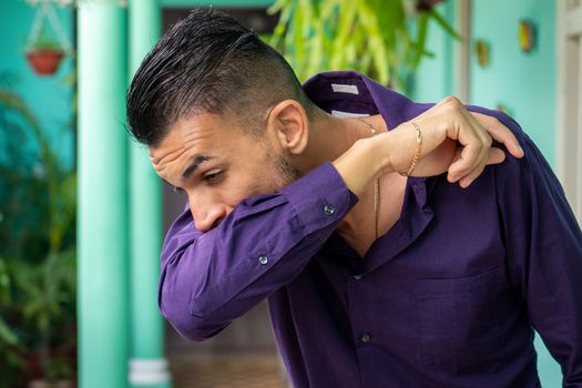 A young man covering his mouth and nose with his bent elbow