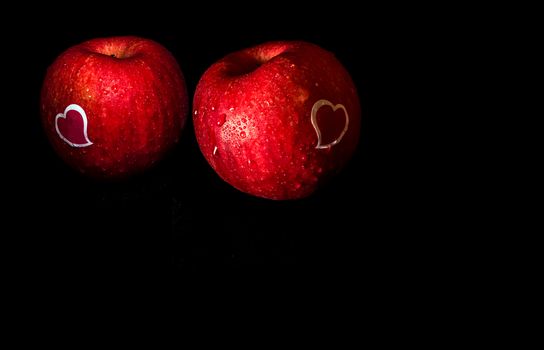 Heart shape sticker and water droplet on glossy surface of freshness red apple on black background