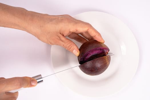 A hand holding a caimito fruit that is being cut with a knife