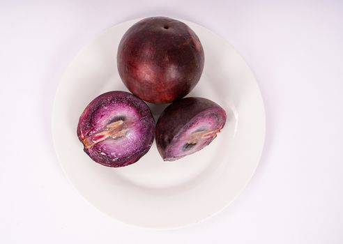 Two caimito fruit on a plate, one of them cut in two