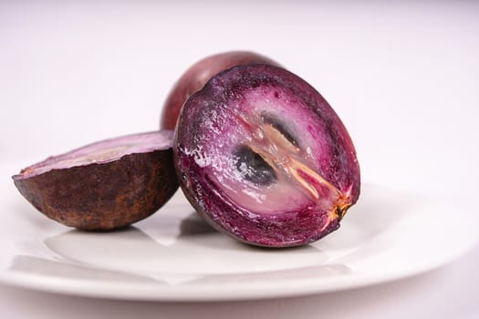 Two caimito fruit on a plate, one of them cut in two pieces