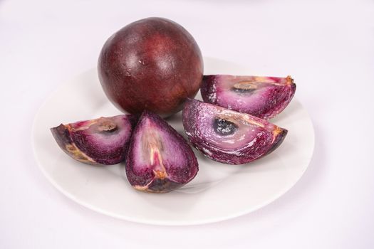 Two caimito fruit on a plate, one of them cut in four pieces