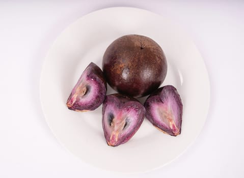 A caimito fruit and three piece of caimito fruit on white plate