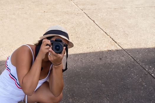A girl wearing hat crouched holding a camera in her hands