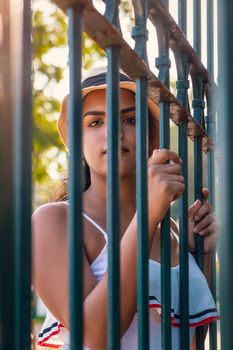 A latin girl wearing hat behind green bars