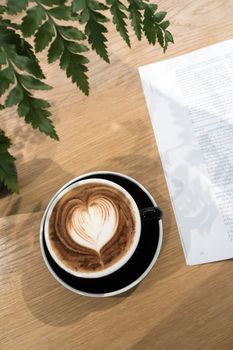 Coffee in black cup with ornament fern and a part of book on wooden table