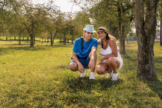 Couple of young people wearing hat crouching in a field with tamarind trees