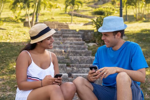 Couple of smiling young people sitting, each with a cellphone in their hands