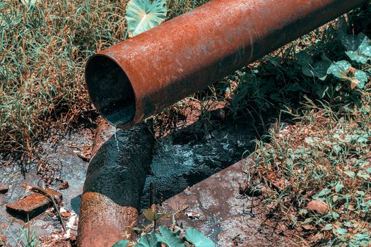 A rusty iron pipe pouring dirty water into a puddle