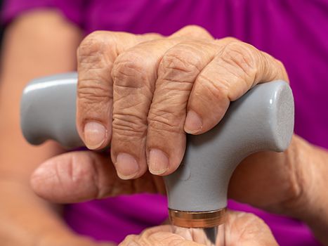 Old wrinkled woman hands holding a walking stick