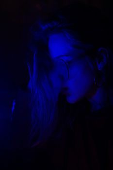 Close up vertical portrait of vaping girl in neon blue light