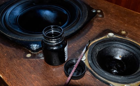 Painting the diffusers of speakers with stamp paint to give them aesthetics. Ink and brush next to the speakers.