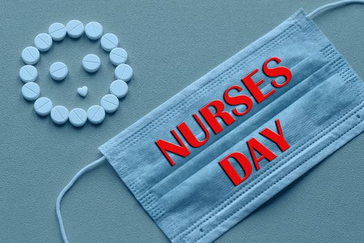 White tablets are arranged in the form of a smiley face on a yellow background. Text of congratulations on the medical holiday nurse's Day. Healthcare and medical concept