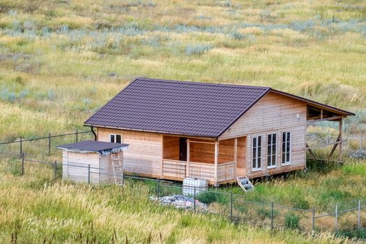 A wooden house made of timber and planks with a roof made of metal. House among the steppe.