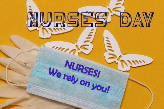 The text of the greeting on the medical holiday-the day of the nurse is written on a blue antiviral bandage, lying on a yellow background next to white butterflies. Healthcare and medical concept