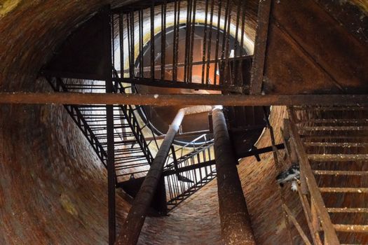 Rusty water tower inside view from top to bottom. Old water pump. Ladder to the water tank, pigeon droppings.