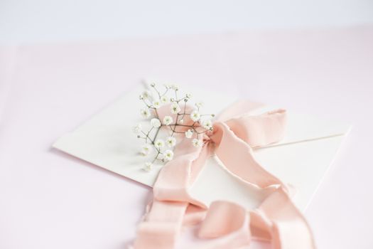 Envelope on a white-pink background with peach silk ribbon and pink flowers. Wedding invitation. Mother's day card. Place for text. Copy space.