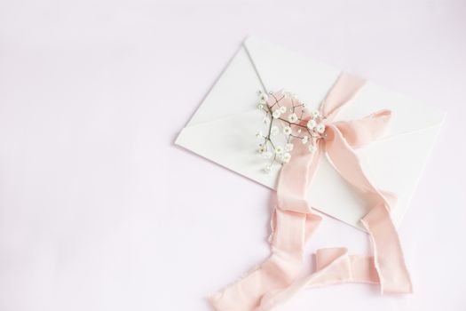 Envelope on a white-pink background with peach silk ribbon and pink flowers. Wedding invitation. Mother's day card. Place for text. Copy space.