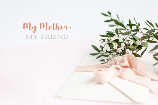 Envelope on a white-pink background with peach silk ribbon, green branch and flowers. Mother's day card.