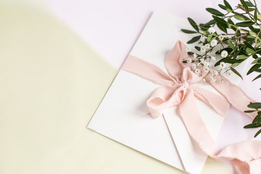 Envelope on a white-pink background with peach silk ribbon, green branch and flowers. Wedding invitation. Mother's day card. Place for text. Copy space.
