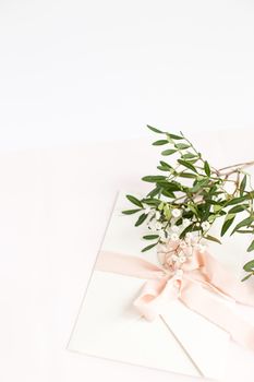 Envelope on a white-pink background with peach silk ribbon, green branch and flowers. Wedding invitation. Mother's day card. Place for text. Copy space.