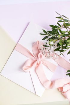 Envelope on a white-pink background with peach silk ribbon, green branch and flowers. Wedding invitation. Mother's day card. Place for text. Copy space.