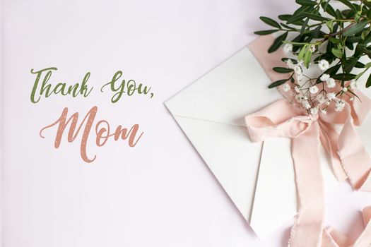 Envelope on a white-pink background with peach silk ribbon, green branch and flowers. Mother's day card.