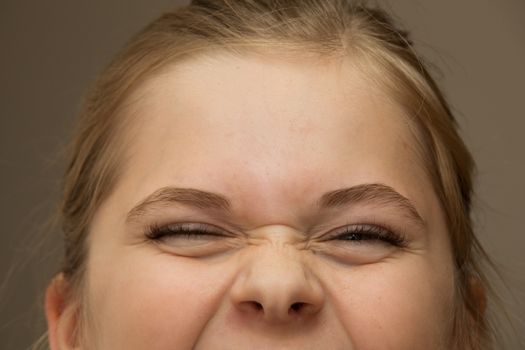 Close up of of a young girl who is squinting while she is smiling or laughing