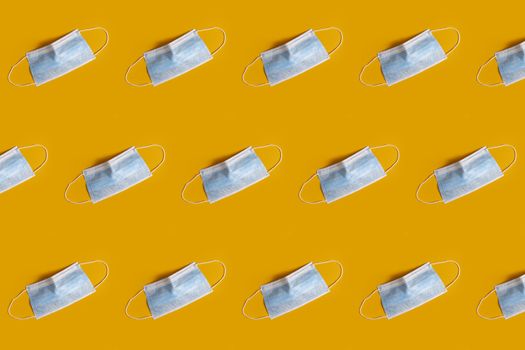 Blue medical masks on the yellow colored background to cover the mouth and nose for protection from virus and bacteria on a yellow background. Epidemic concept. Regular pattern, flat lay.