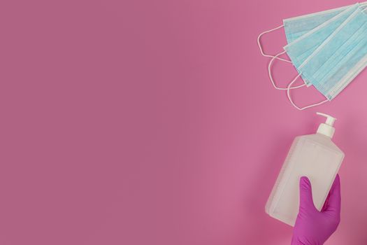 Doctor holds sanitizer gel in hands pink medical gloves. Respiratory surgical face mask  on pink background. Pandemic corona virus, insurance, airborne diseases, SARS, grippe. 